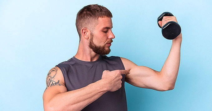 A fit man curling a dumbbell | Trainest 