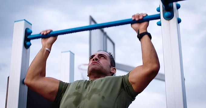 A close-up of a fit man doing pull-ups | Trainest
