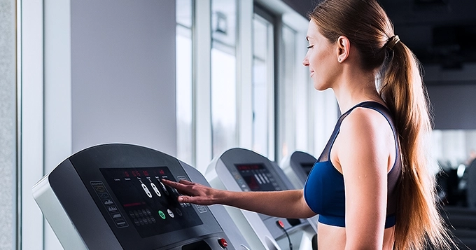 A woman at the gym setting the treadmill | Trainest