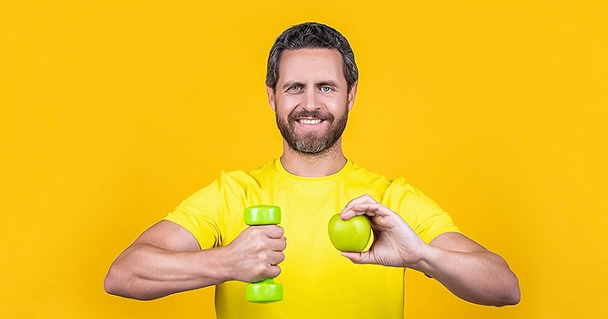 A man with an apple in one hand and a dumbbell in the other | Trainest
