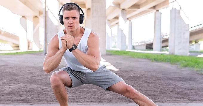 A fit man doing exercise outdoors while wearing smart watch and headphones | Trainest