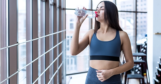 A woman in workout attire drinking from a tumbler | Trainest