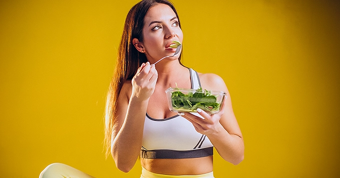 A woman in workout clothes eating salad | Trainest
