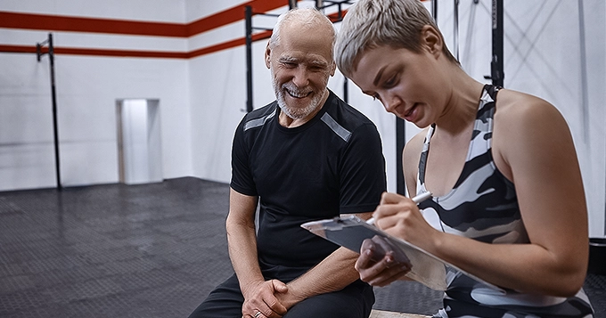 A middle-aged person talking to a fitness trainer at the gym | Trainest
