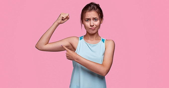 A slim woman flexing her muscles | Trainest
