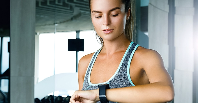 A woman in workout clothes looking at her smart watch | Trainest
