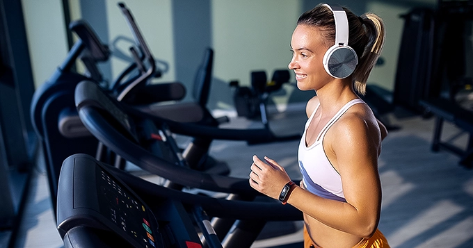A woman with headphones on running on a treadmill | Trainest

