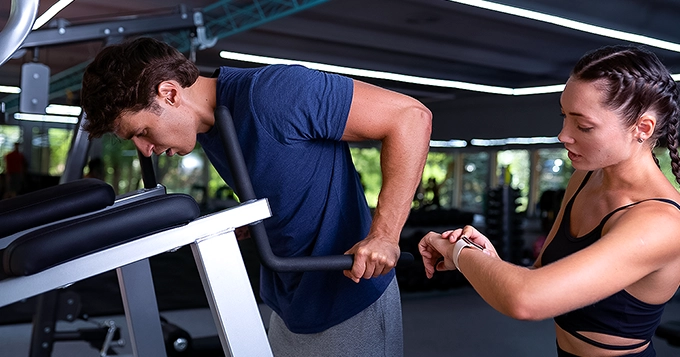A personal trainer looking at watch while client is doing an exercise | Trainest