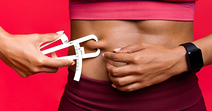 A moderately fit person using body fat caliper on her stomach | Trainest