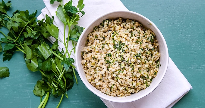 A bowl filled with fluffy cooked brown rice, garnished with a little parsley or cilantro for added color | Trainest
