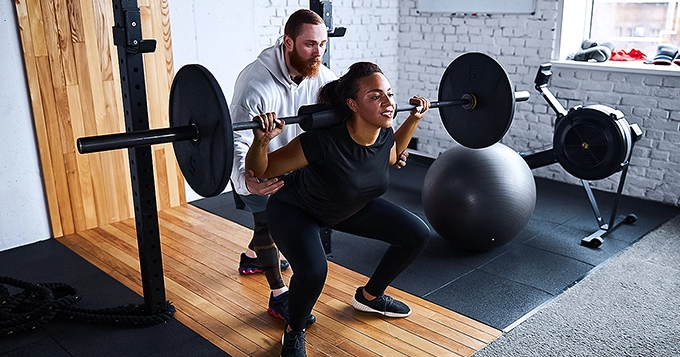 A fitness trainer helping someone to do the proper form squat | Trainest