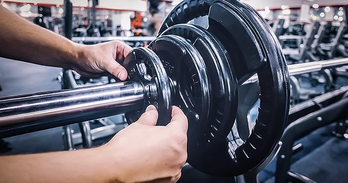 Someone adjusting weights on a barbell in a gym | Trainest