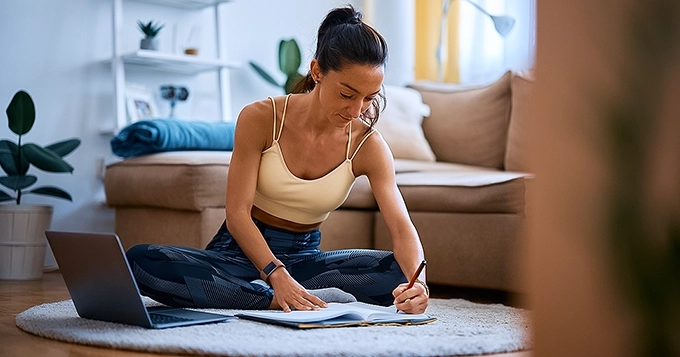 An image of a person writing or reviewing a fitness and recovery plan in a journal or planner | Trainest